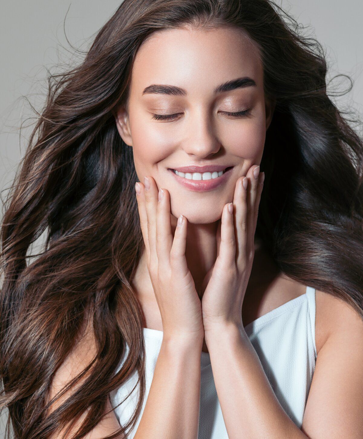 Smiling woman with flowing hair and hands on face.