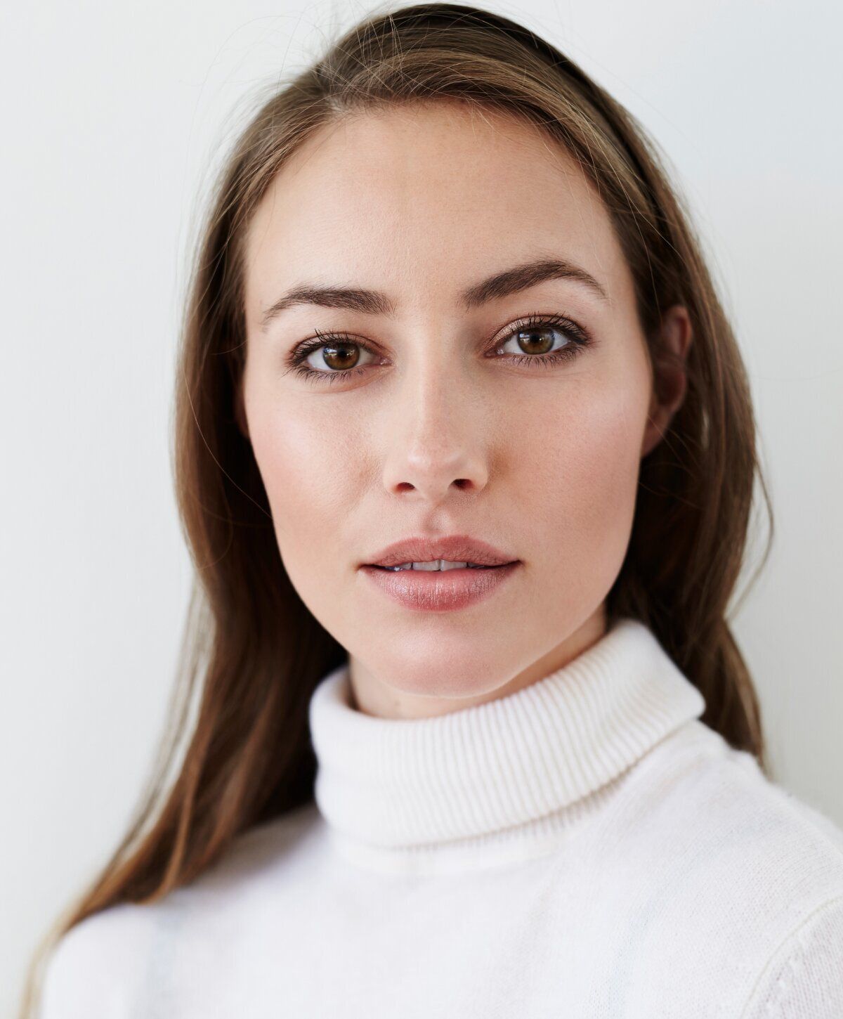Woman in a white turtleneck sweater, neutral background.
